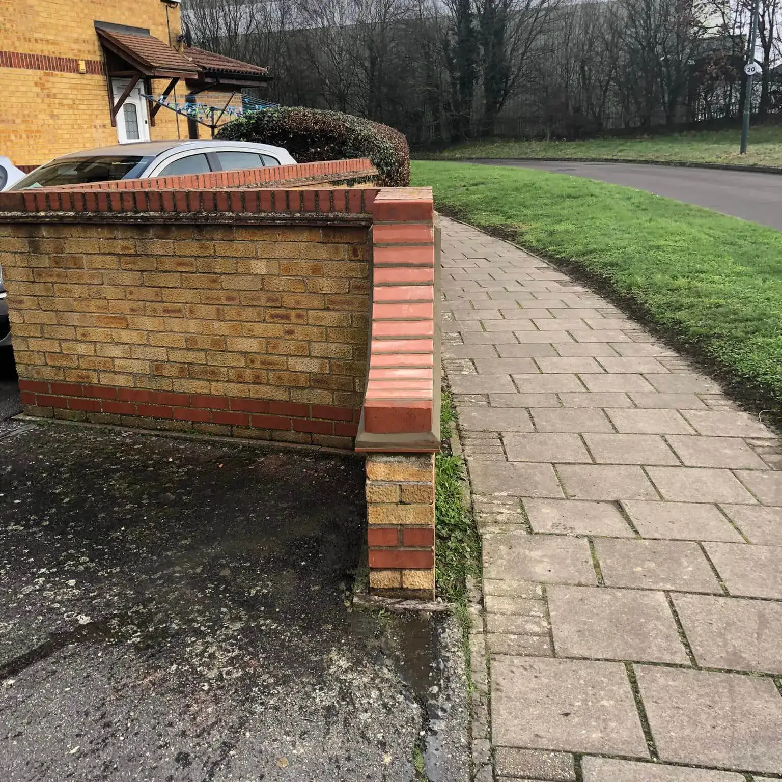 a brick wall next to a car parked on the side of a road